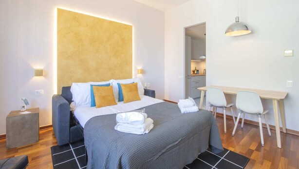 A modern hotel room with a large bed, bedside lamps, a desk, and a chair. - Sweett | Torre Velasca VII (Milano)