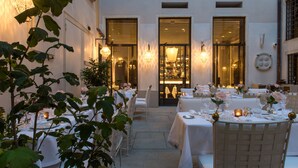 An outdoor dining area with tables set for a meal, surrounded by white walls and large windows. - Nolinski Venezia - Evok Collection (Venice)