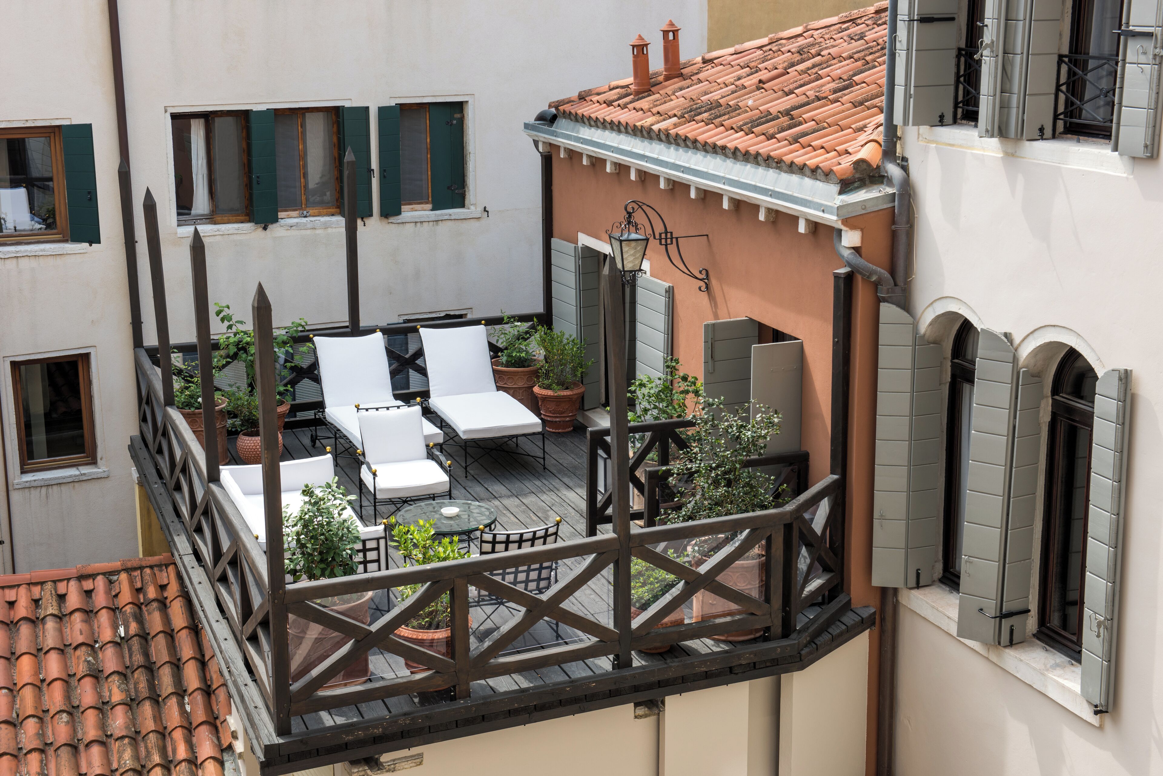 A rooftop terrace with outdoor seating, potted plants, and a view of adjacent buildings.
