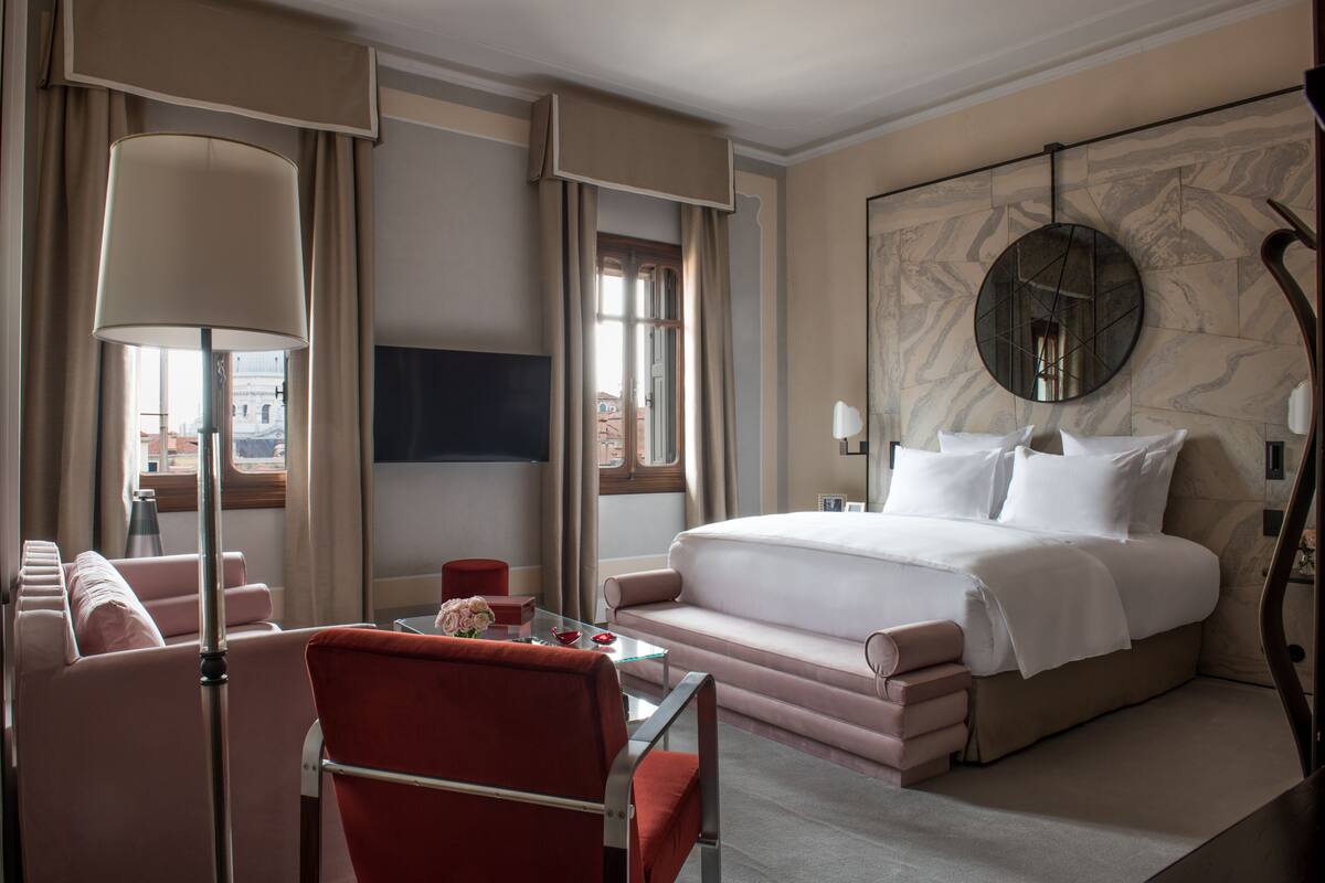 A hotel room with a bed, a sofa, a table, a lamp, and a wall-mounted TV.