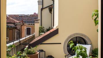 A balcony with a table, chairs, potted plants, and a view of neighboring buildings.