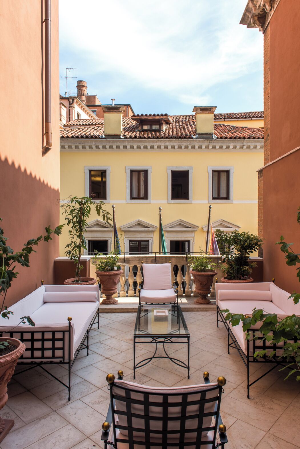Un cortile con un tavolo in vetro, due poltrone imbottite e piante in vaso.