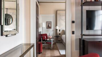 Corridoio di un hotel con ringhiera in vetro, una sedia rossa, un tavolino con un vaso e un letto con un comodino.
