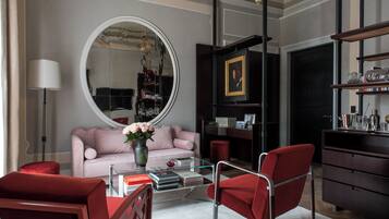 Una sala de estar moderna con un espejo redondo, un sofá rosa, sillas rojas, una mesa de centro de vidrio y una estantería de madera oscura.