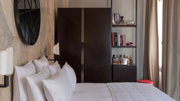 Een hotelkamer met een bed, een boekenkast, een spiegel en een rode poef.