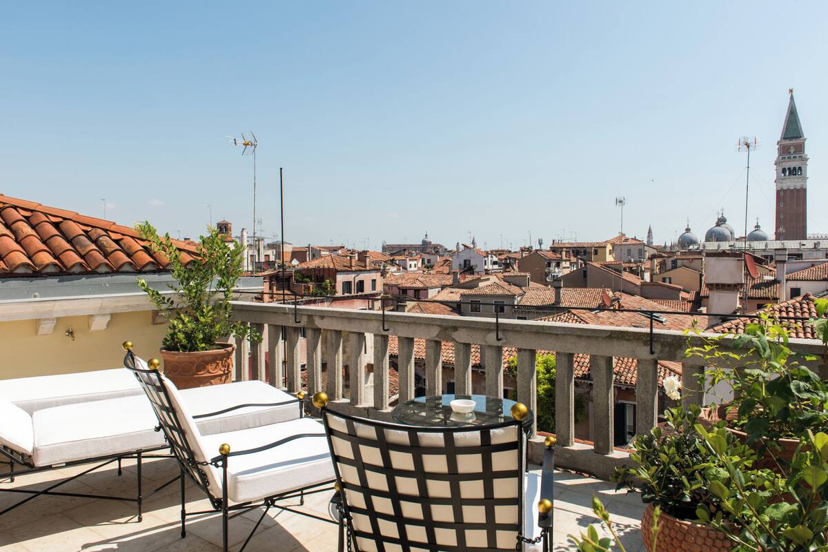A terrace with a table and chairs, overlooking a cityscape with buildings and a tower.