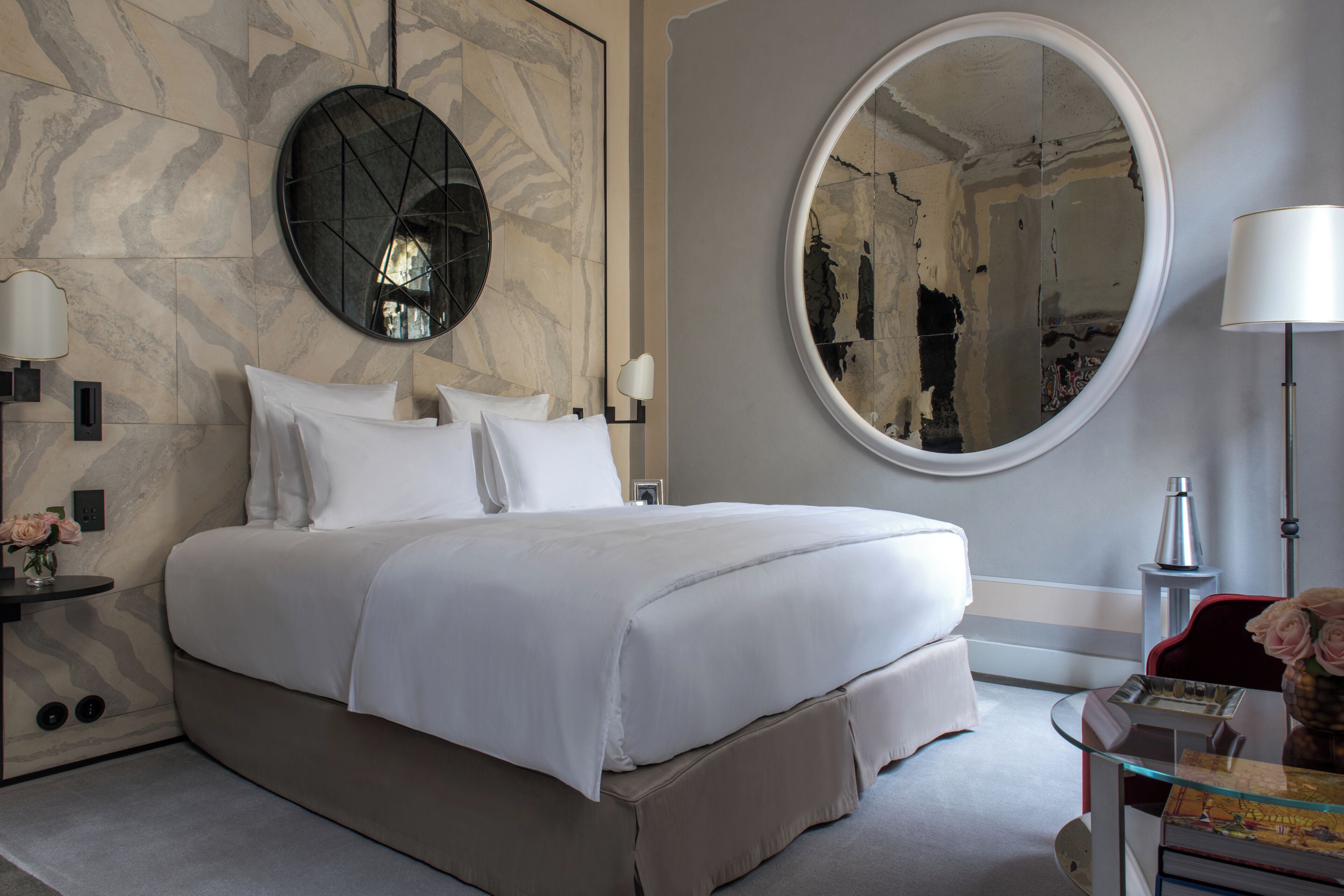 A modern hotel room with a large bed, a round mirror, a round table, and a red chair.