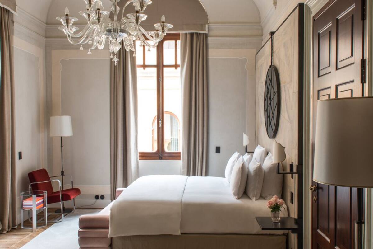Ein geräumiges Schlafzimmer mit einem großen Bett, einer Kristalllüster, einem roten Sessel und einem Holzboden im Fischgrätmuster.