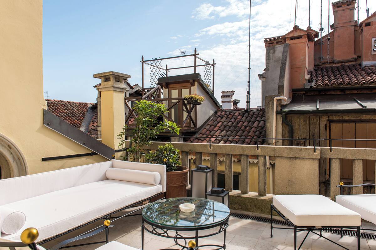 A rooftop terrace with a white sofa, a glass table, and a potted plant.