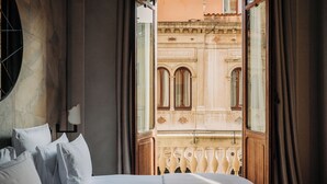 A hotel room with a bed, a window with curtains, and a view of a building with ornate architecture. - Nolinski Venezia - Evok Collection (Venice)