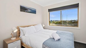 Ein Schlafzimmer mit einem Bett, einem Nachttisch, einer Schreibtischlampe, einem Fenster mit Ausblick und einem Deckenventilator.