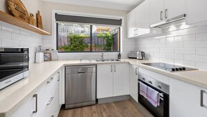 Eine moderne Küche mit weißen Schränken, Edelstahlgeräten, einem Geschirrspüler und einem Fenster mit Blick auf einen Garten.