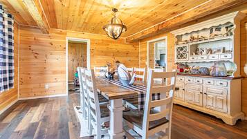 Un intérieur en bois comprenant une table à manger, des chaises, un lustre et un buffet blanc agrémenté d’objets décoratifs.
