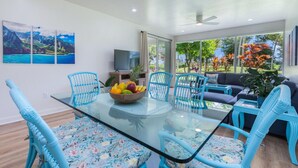Een moderne woonkamer met een eettafel met glazen blad, omringd door blauwe stoelen, een bank en een televisie.