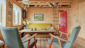 Un intérieur en bois comprenant une table à manger, des chaises, un banc, un lustre et une porte rouge.