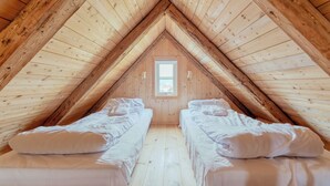 Une petite chambre mansardée avec deux lits simples, des poutres en bois et une fenêtre.