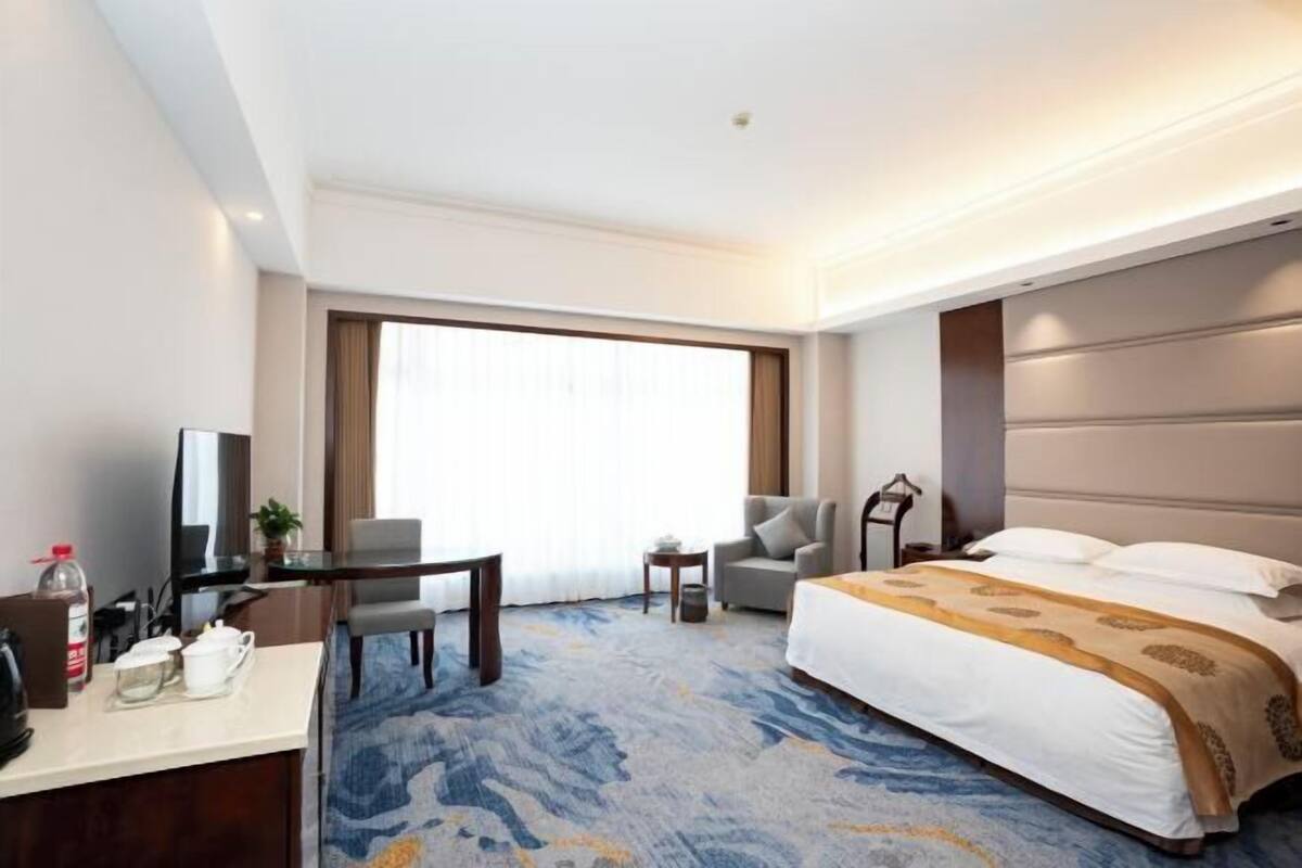 A hotel room with a bed, a desk, a chair, a television, and a window with curtains.