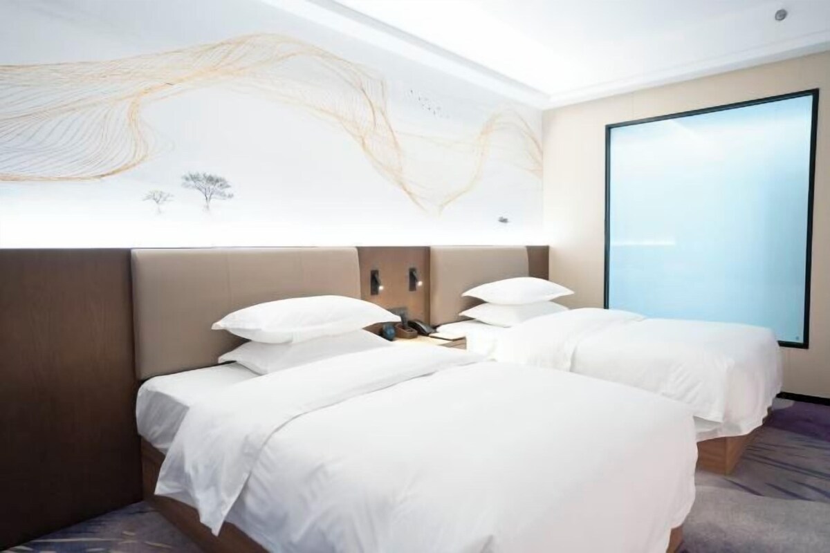 Habitación de hotel con dos camas, un ventanal grande y un mural en la pared.