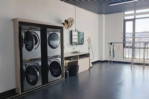 Une buanderie équipée de quatre machines à laver, d’un évier et d’une fenêtre laissant entrer la lumière naturelle.