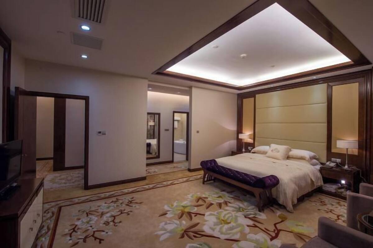 A hotel room with a large bed, a television, a desk, and a bathroom visible through an open door.