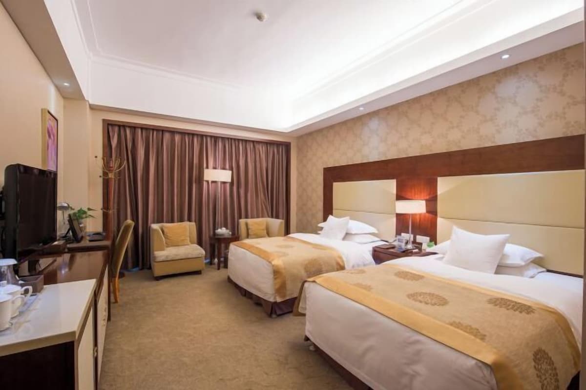 A hotel room with two beds, a desk, a chair, a TV, and a window with curtains.
