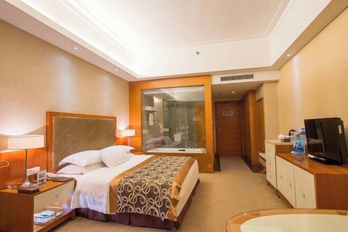 A hotel room with a bed, bedside table, lamp, TV, and a bathroom with a shower and toilet.