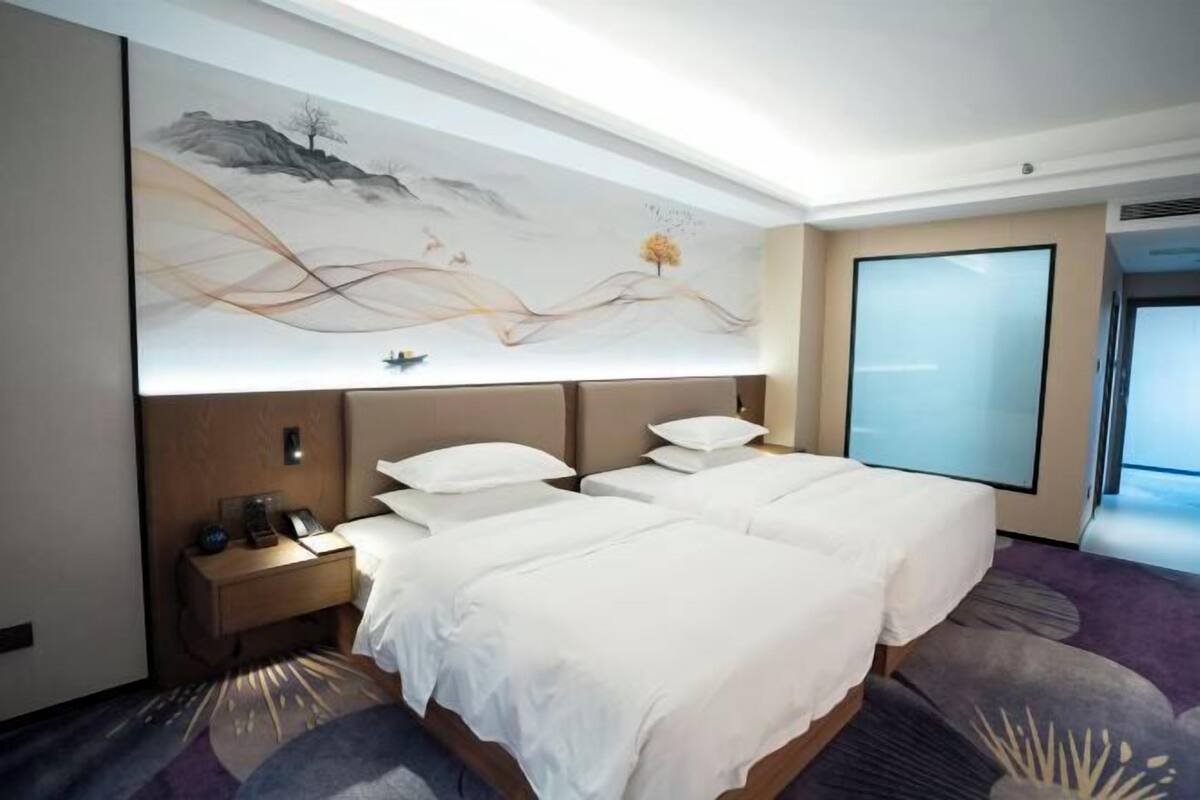 A hotel room with a large bed, a nightstand, a wall-mounted TV, and a large window.