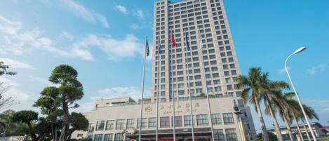 Un hotel alto con fachada moderna, asta de bandera y un jardín bien cuidado.