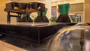 Un piano à queue sur une scène dotée d’un sol en marbre, entouré d’un escalier et d’éléments décoratifs verts.