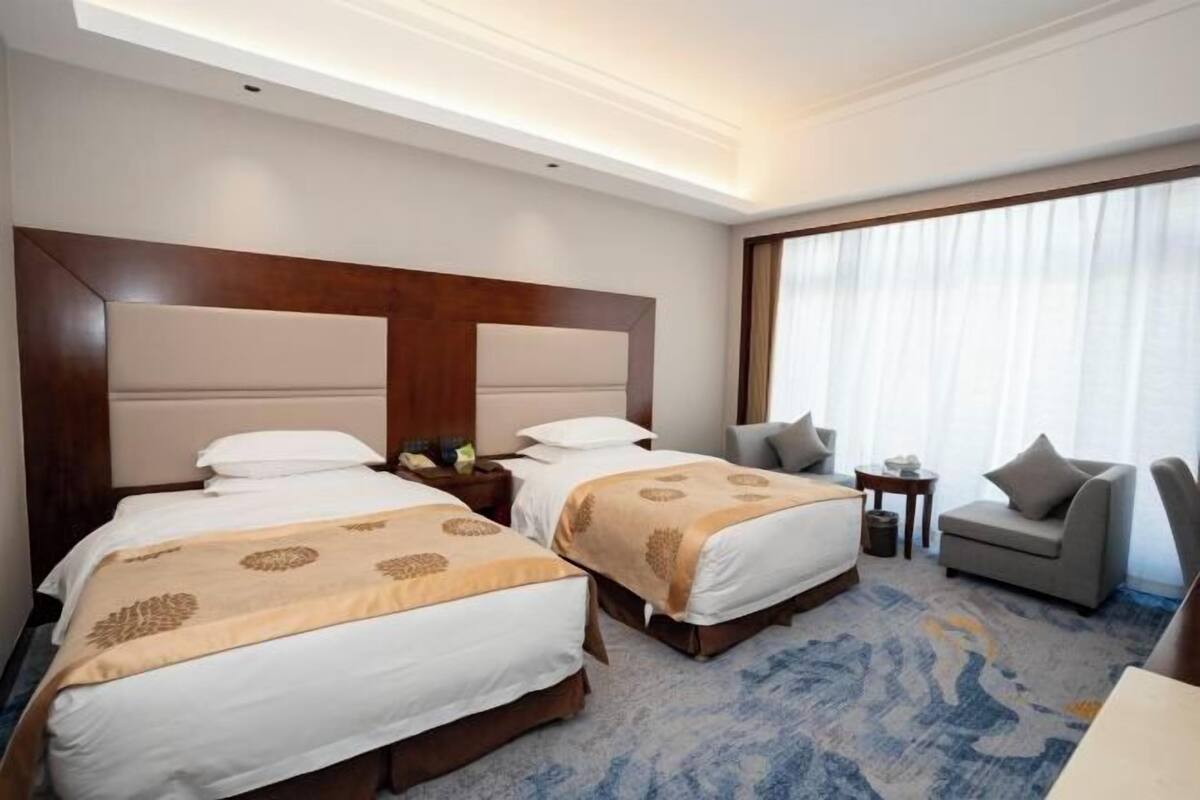 A hotel room with two beds, a sofa, a small table, and a large window with curtains.