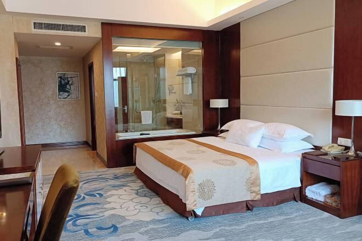 A hotel room with a bed, bedside table, lamp, and a mirror.
