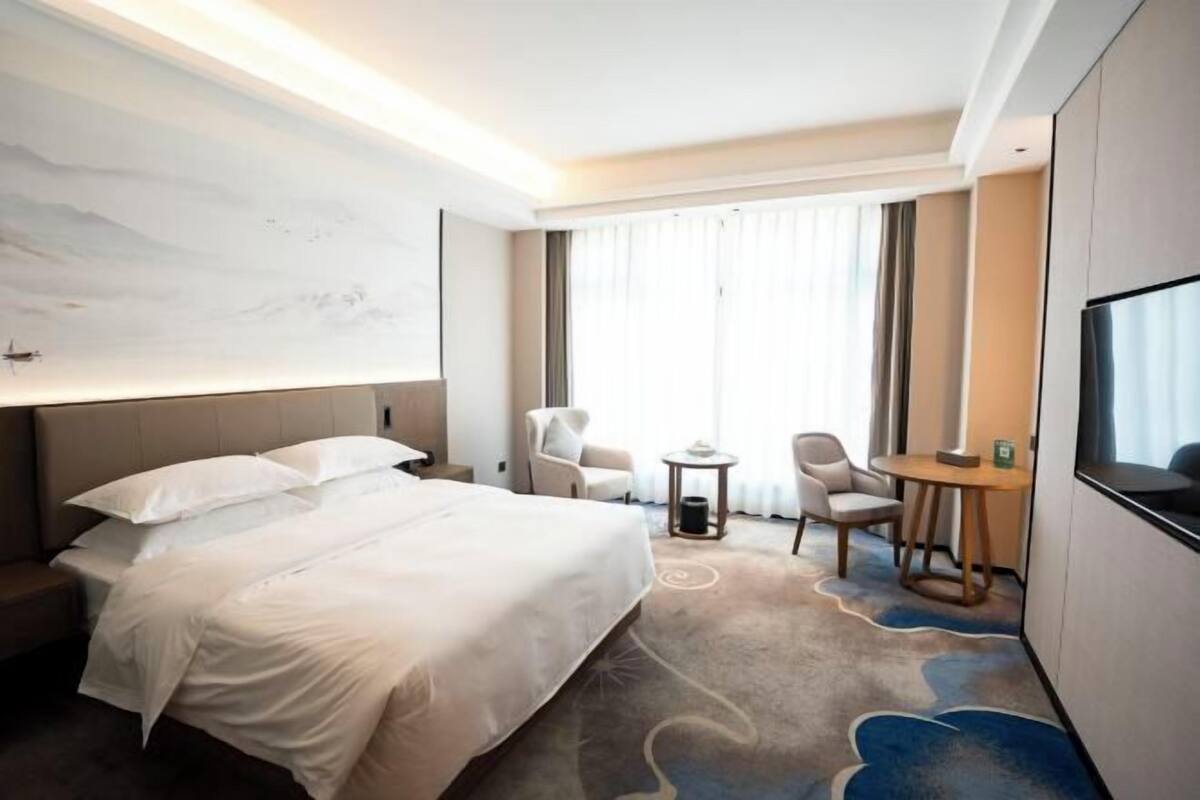 A hotel room with a large bed, two chairs, a small table, and a TV.