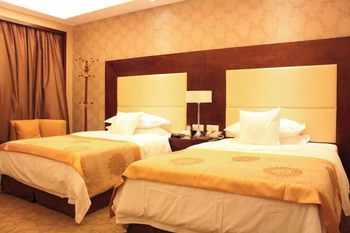 A hotel room with two beds, a nightstand, a lamp, and a decorative item on the wall.
