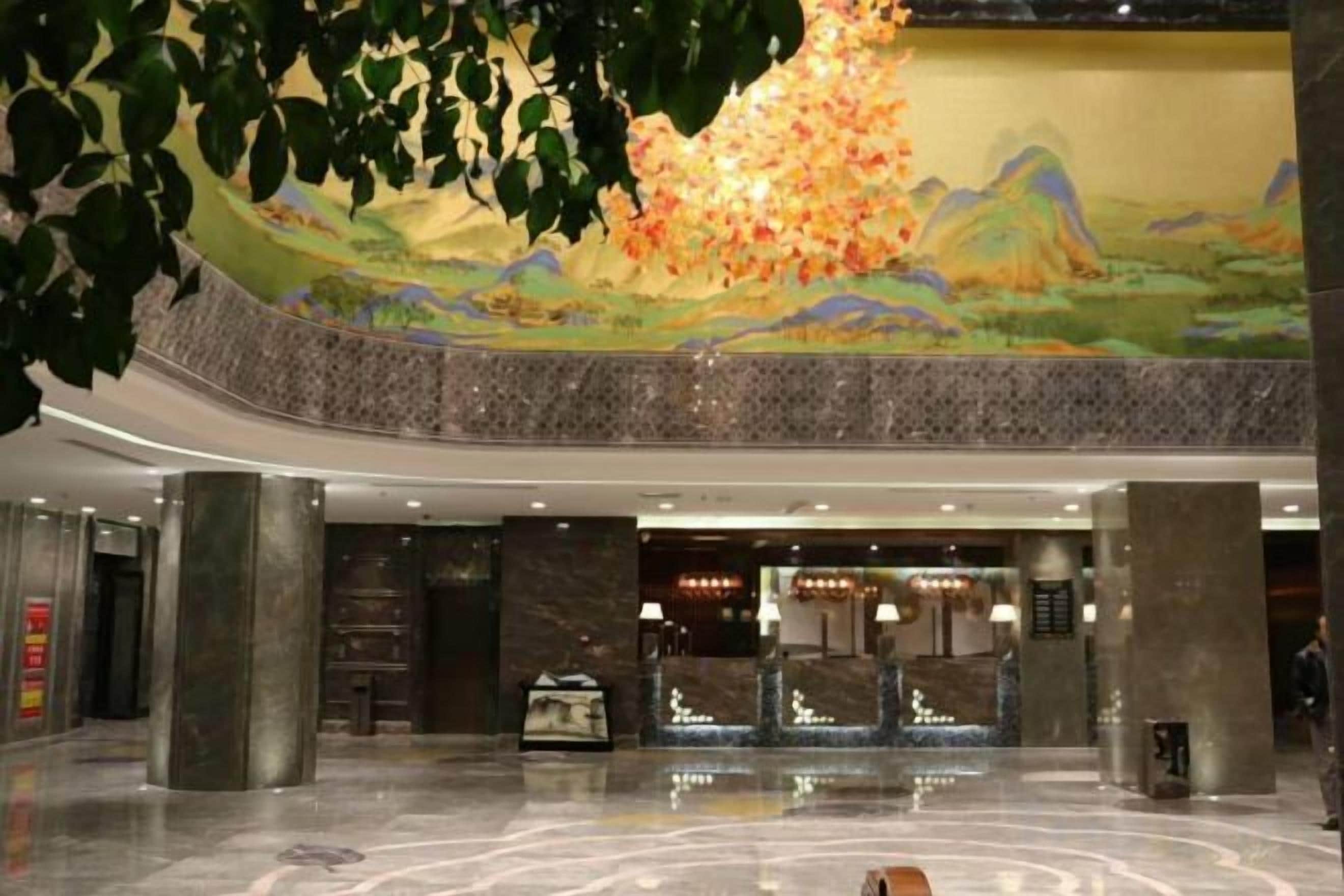 A hotel lobby with a reception desk, a large mural, and a marble floor.