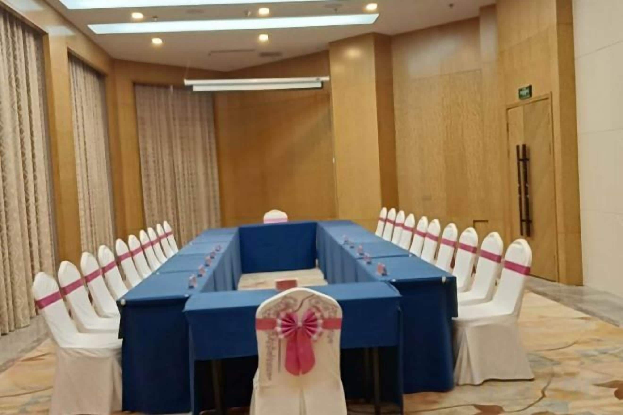 A conference room with a long table, white chairs with pink sashes, and a blue tablecloth.