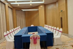 Een vergaderzaal met een lange tafel, witte stoelen met roze linten en een blauwe tafelkleed.