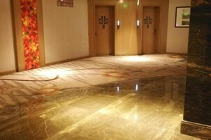A hotel corridor with a polished marble floor, wooden doors, and a wall with a floral pattern.
