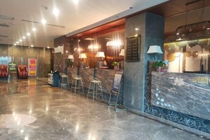 Un espace d’accueil d’hôtel doté d’un comptoir en marbre, de sièges de bar et de luminaires modernes.