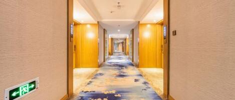 A hotel corridor with a carpeted floor, wooden walls, and a ceiling light fixture.