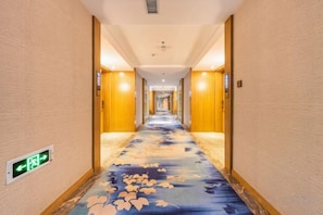 Corredor de hotel com piso de carpete, paredes de madeira e luminária no teto.