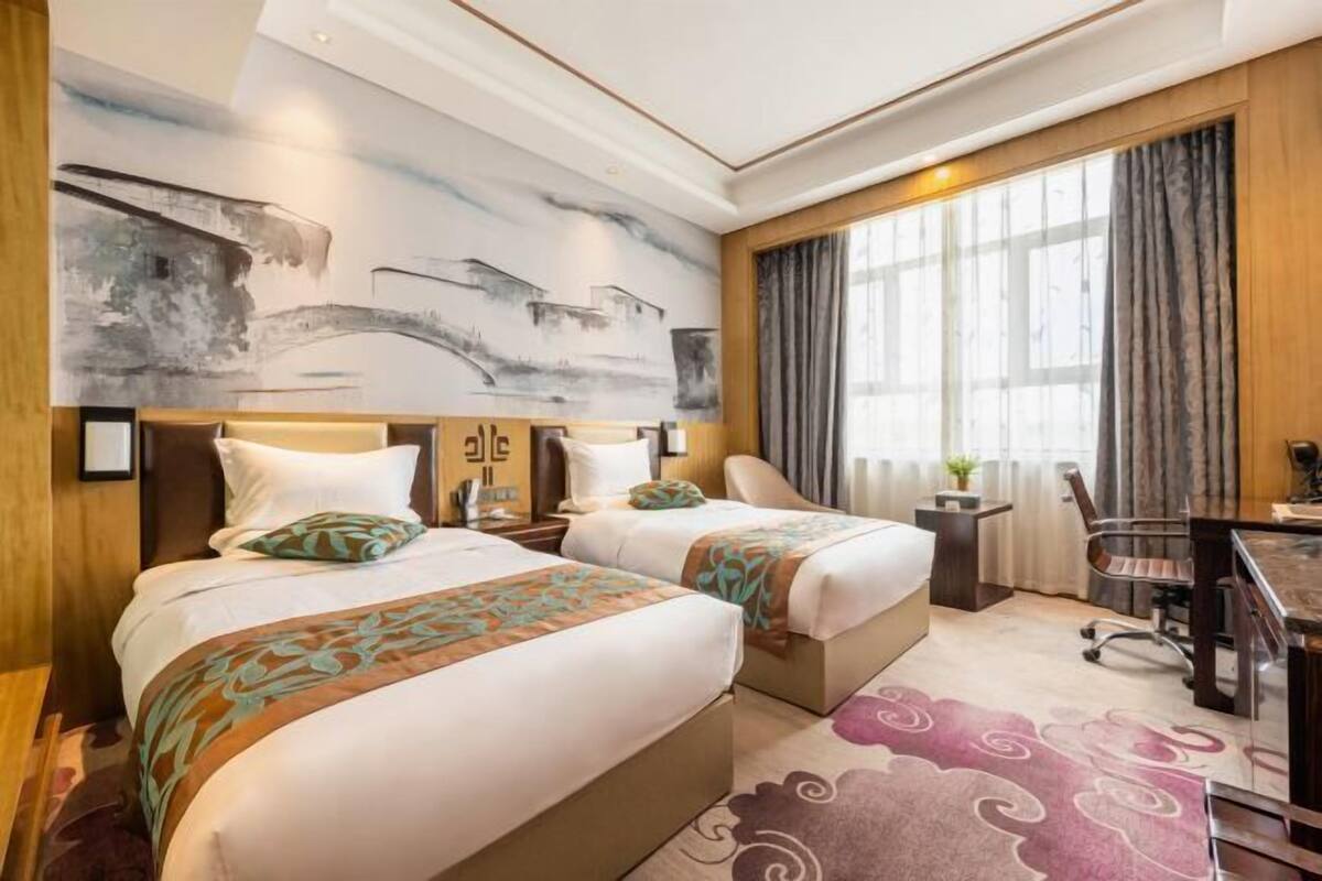 Ein Hotelzimmer mit zwei Betten, einem Schreibtisch, einem Stuhl und einem großen Fenster mit Vorhängen.