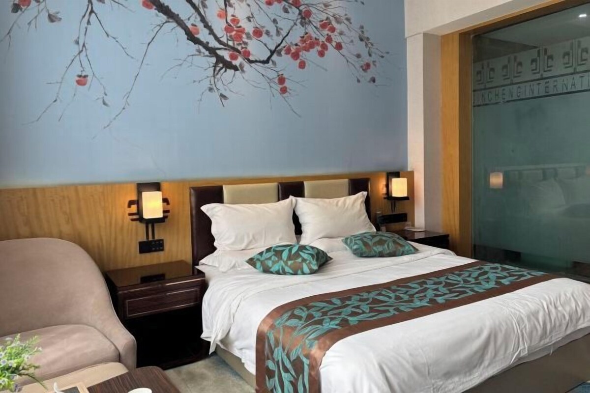 Een hotelkamer met een bed, nachtkastjes, een stoel en een muur met een geschilderde tak.