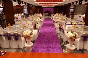 Un salón de banquetes con mesas redondas, centros de mesa con flores moradas y una alfombra púrpura.