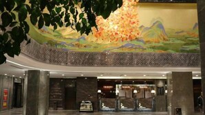 Un hall d’entrée spacieux, orné d’une grande fresque murale, de colonnes en marbre et d’un comptoir d’accueil.