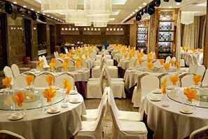 Een balzaal met ronde tafels, ingericht voor een formeel evenement, met witte stoelen en tafels met witte tafelkleden.