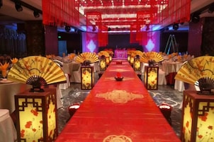 Un salón de banquetes con alfombra roja, mesas con manteles blancos y faroles tradicionales.