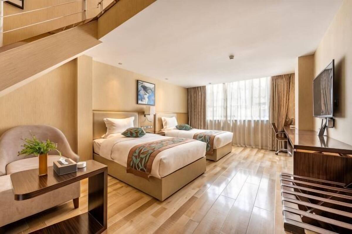 Ein Hotelzimmer mit zwei Betten, einem Schreibtisch, einem Stuhl, einem Fernseher und einer Treppe.