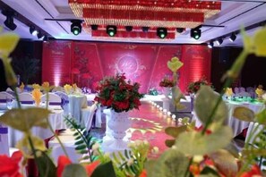 Een feestzaal met ronde tafels, bloemrijke decoraties en een podium met rode achtergrond.