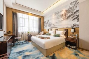 Een hotelkamer met een groot bed, een bureau, een stoel, een televisie en een groot schilderij aan de muur.