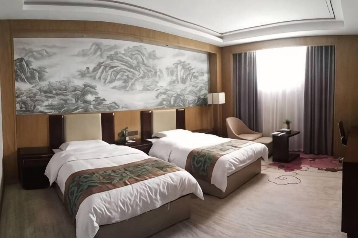 Ein Hotelzimmer mit zwei Betten, einem großen Wandbild, einem Sessel, einem Schreibtisch und einem Fenster mit Vorhängen.